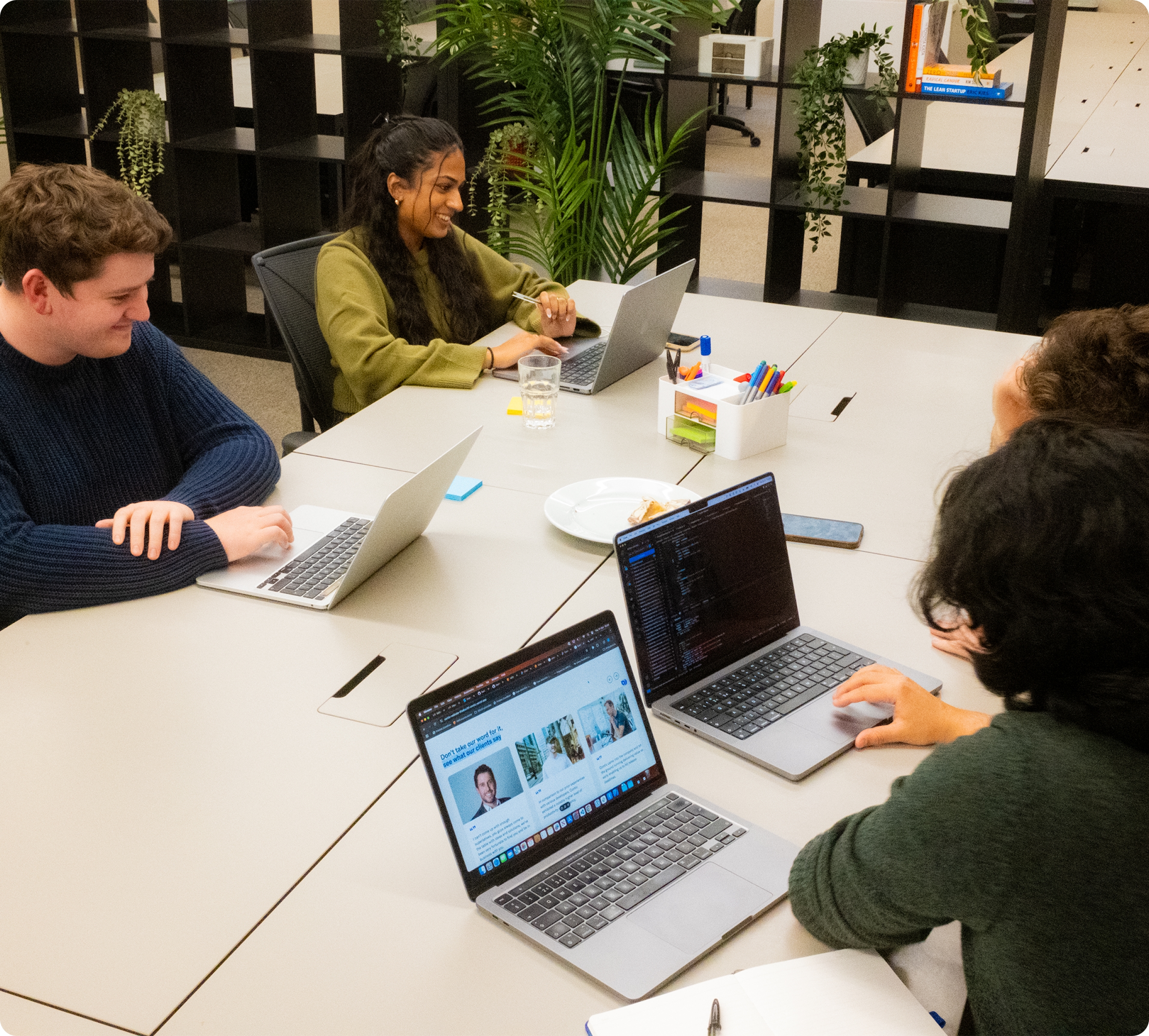 Four people collaborating at a table with laptops in a modern office setting.