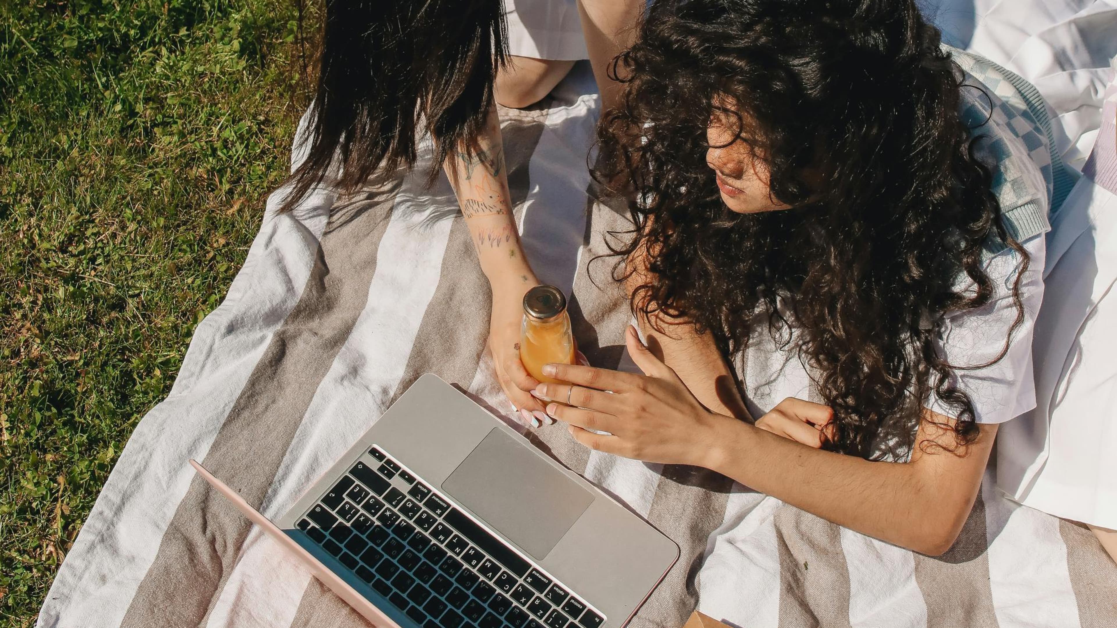 Two people laying on a blanket in a field, looking at a laptop