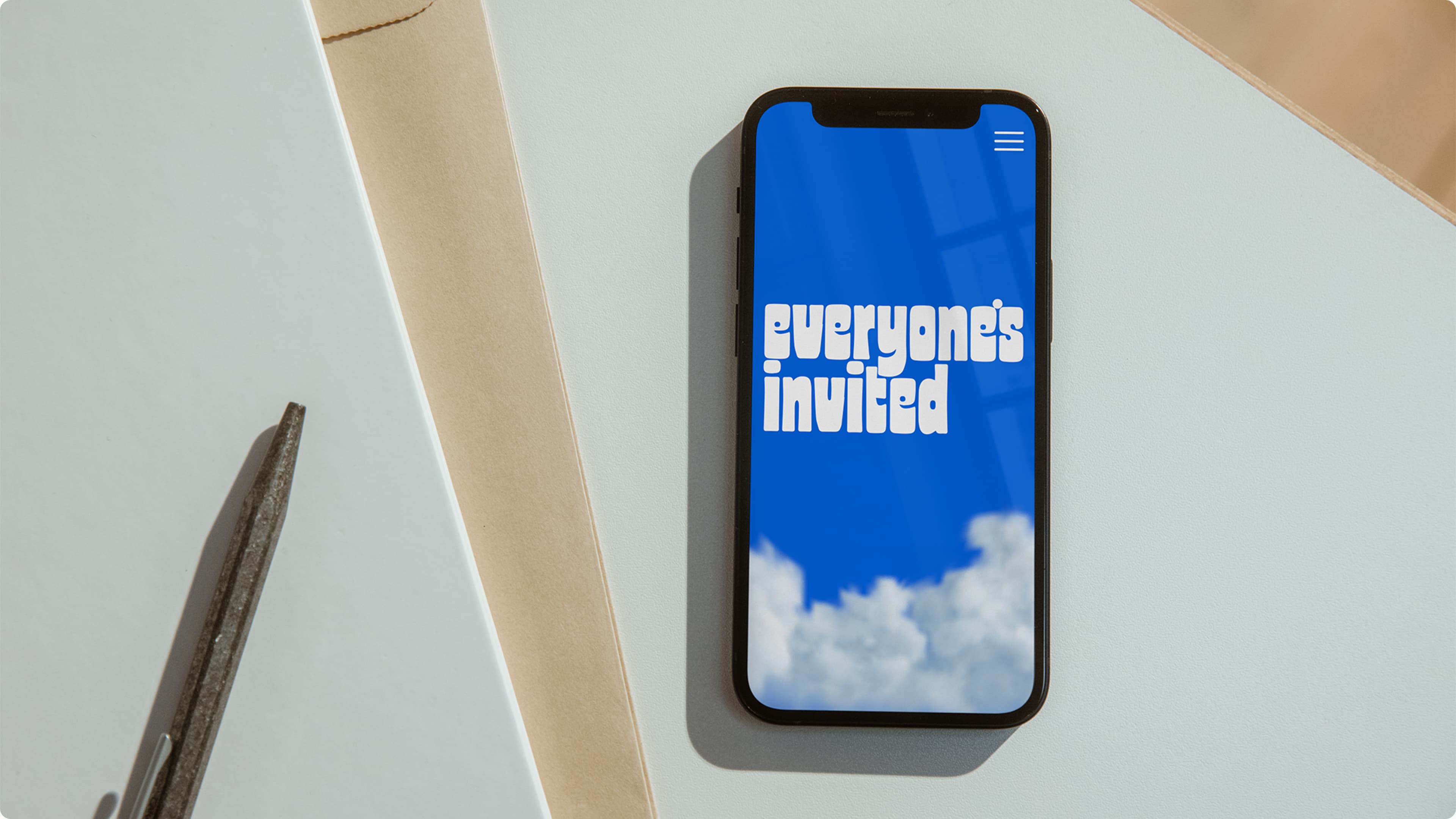 a smartphone on top of a stack of paper displaying the everyones invited logo on a blue background