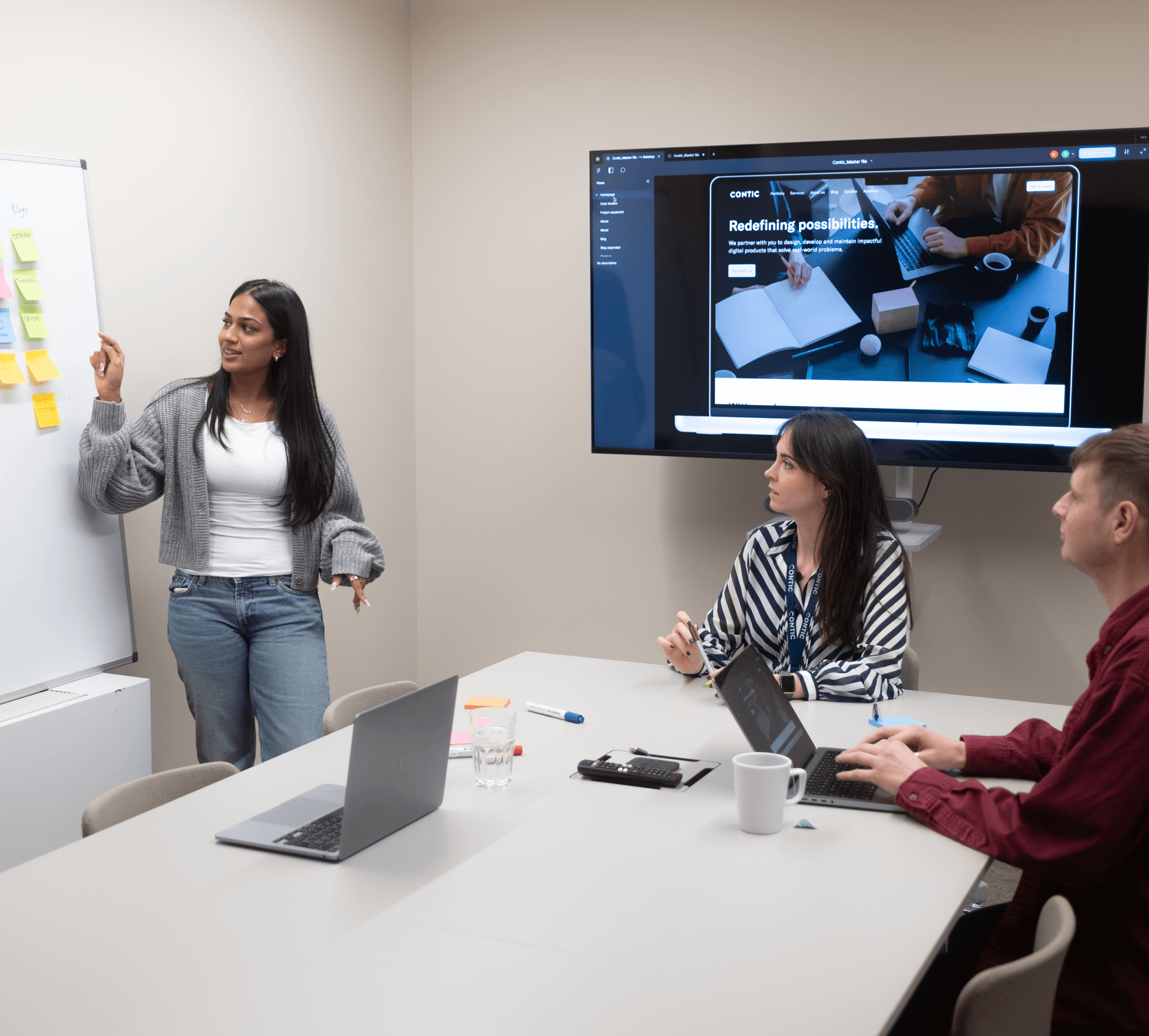 Two people around a table looking at a third person presenting plans on a large whiteboard